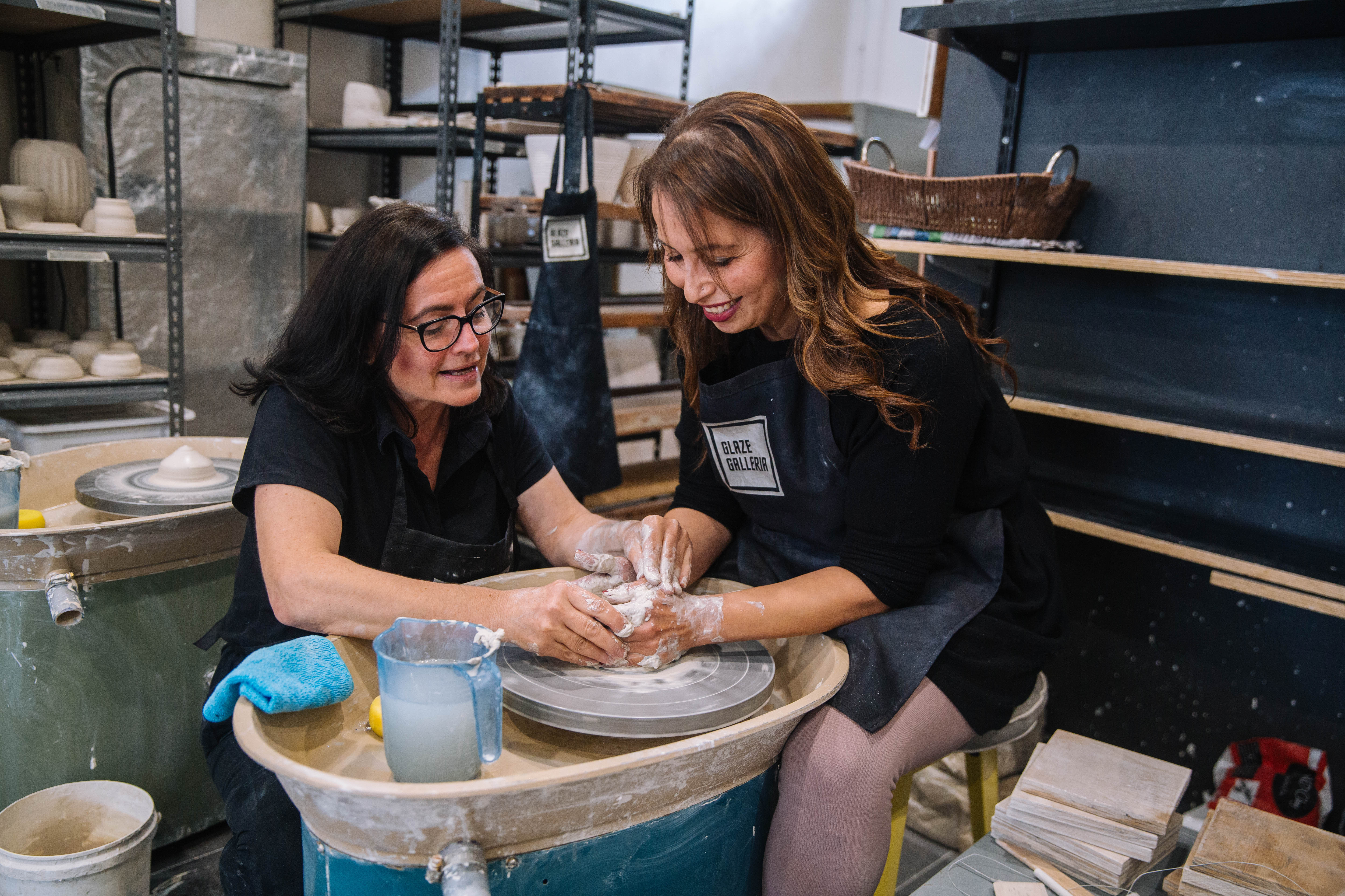Teacher helping a student shape their clay on a pottery wheel